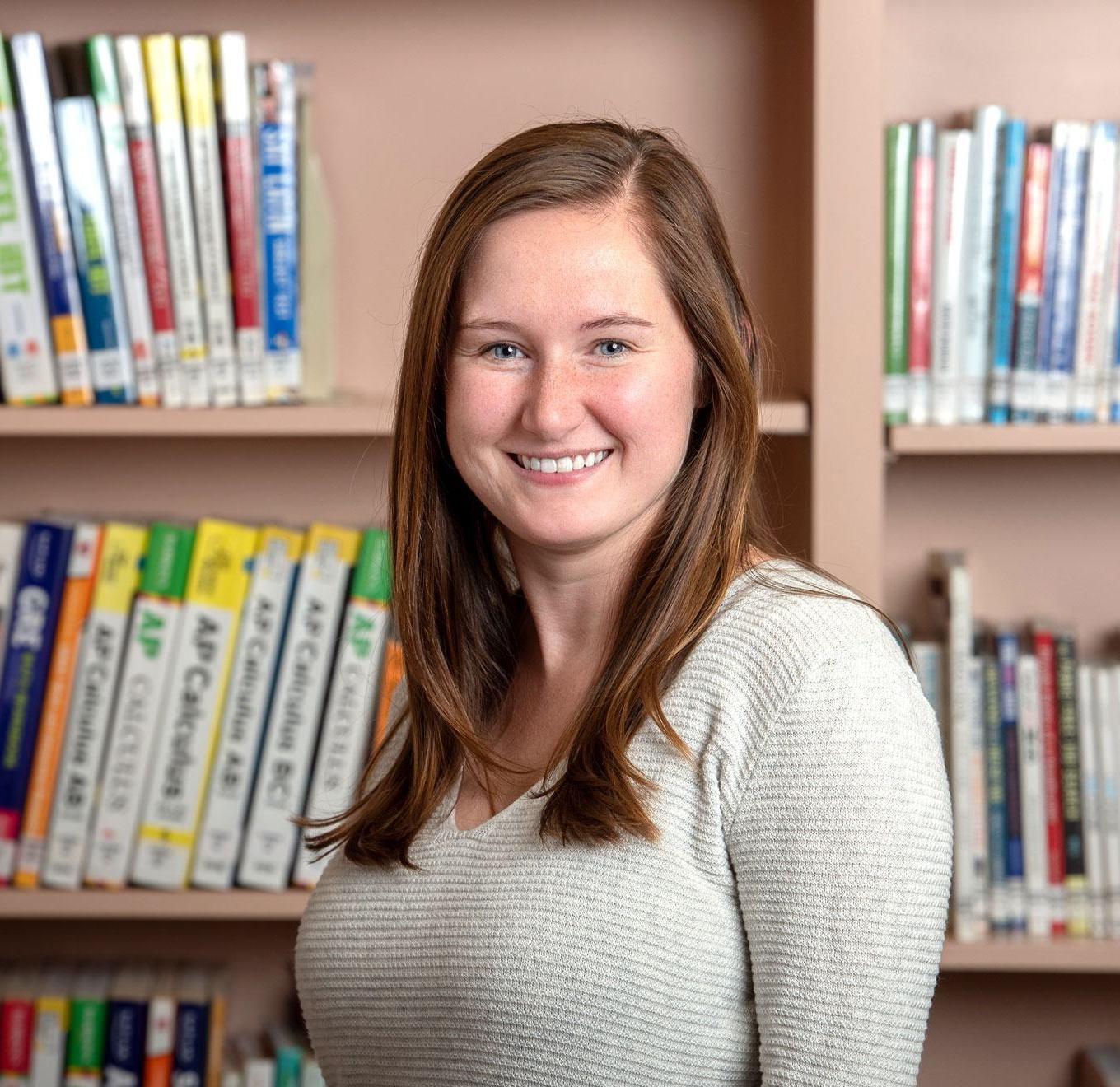 A headshot of Megan in her school library. She has long hair and is wearing a long-sleeved beige shirt.