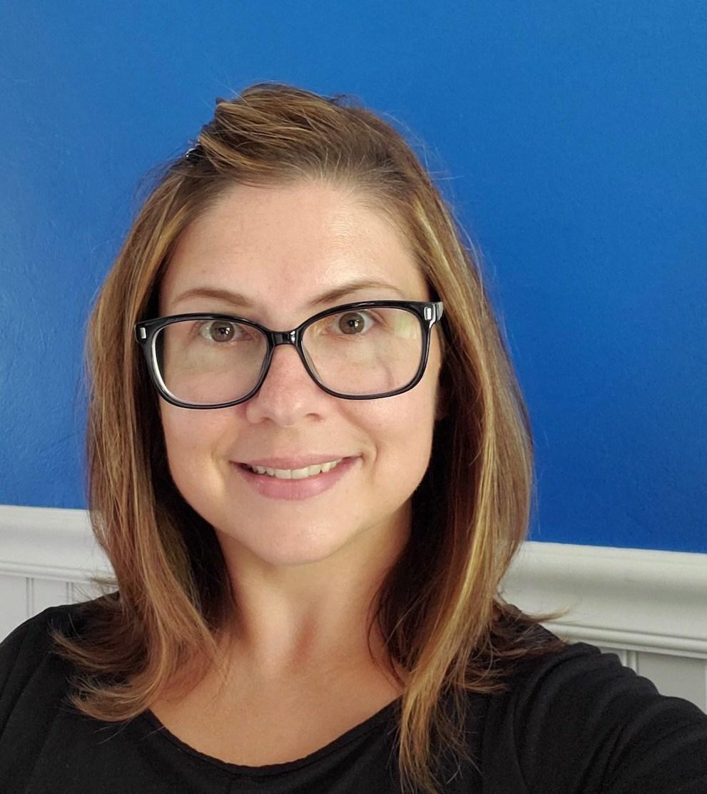 A photo of Melissa, a teacher with shoulder-length hair and glasses and is smiling against a blue background.
